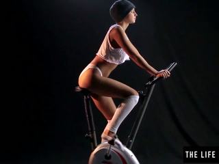 প্রেমময় ঘর্মাক্ত বালিকা পিঠ বাঁকানো একটি exercise bike আসন.